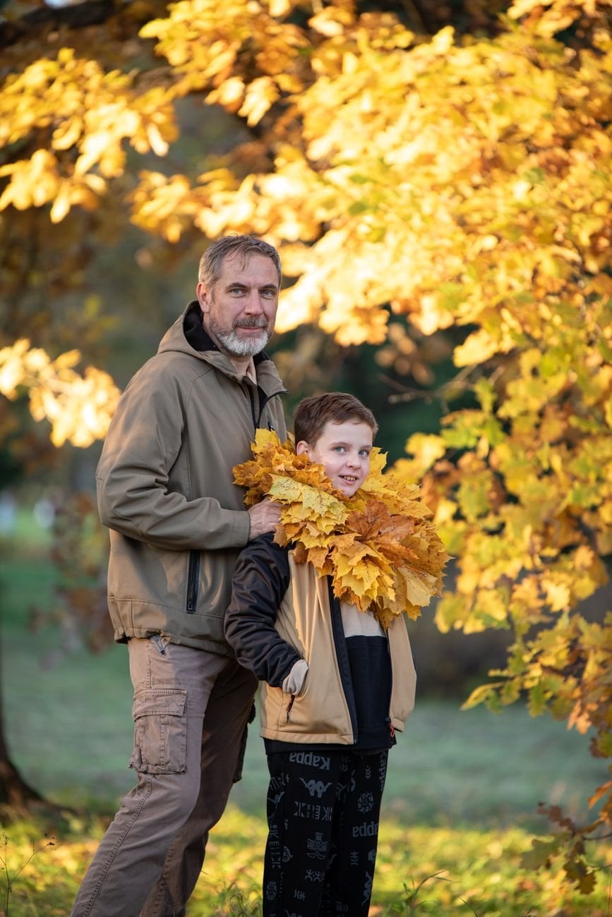 Father and son bonding amid vibrant autumn leaves. Warm family moment captured outdoors.